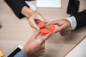 Zwei Personen setzen ein orangenes Kreisdiagramm aus Holzteilen zusammen, Symbol für Teamarbeit und Strategie