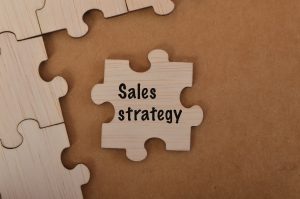Holzpuzzleteil mit der Aufschrift 'Sales strategy' als Symbol für Vertriebsstrategie