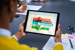 Person hält ein Tablet mit einer Grafik zur Marketing-Strategie, aufgeführt sind Branding, Social Media, Viral Content, SEO und Ads