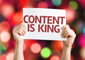 Zwei Hände halten ein weißes Schild mit dem Schriftzug „Content is King" vor buntem, unscharfem Lichterhintergrund