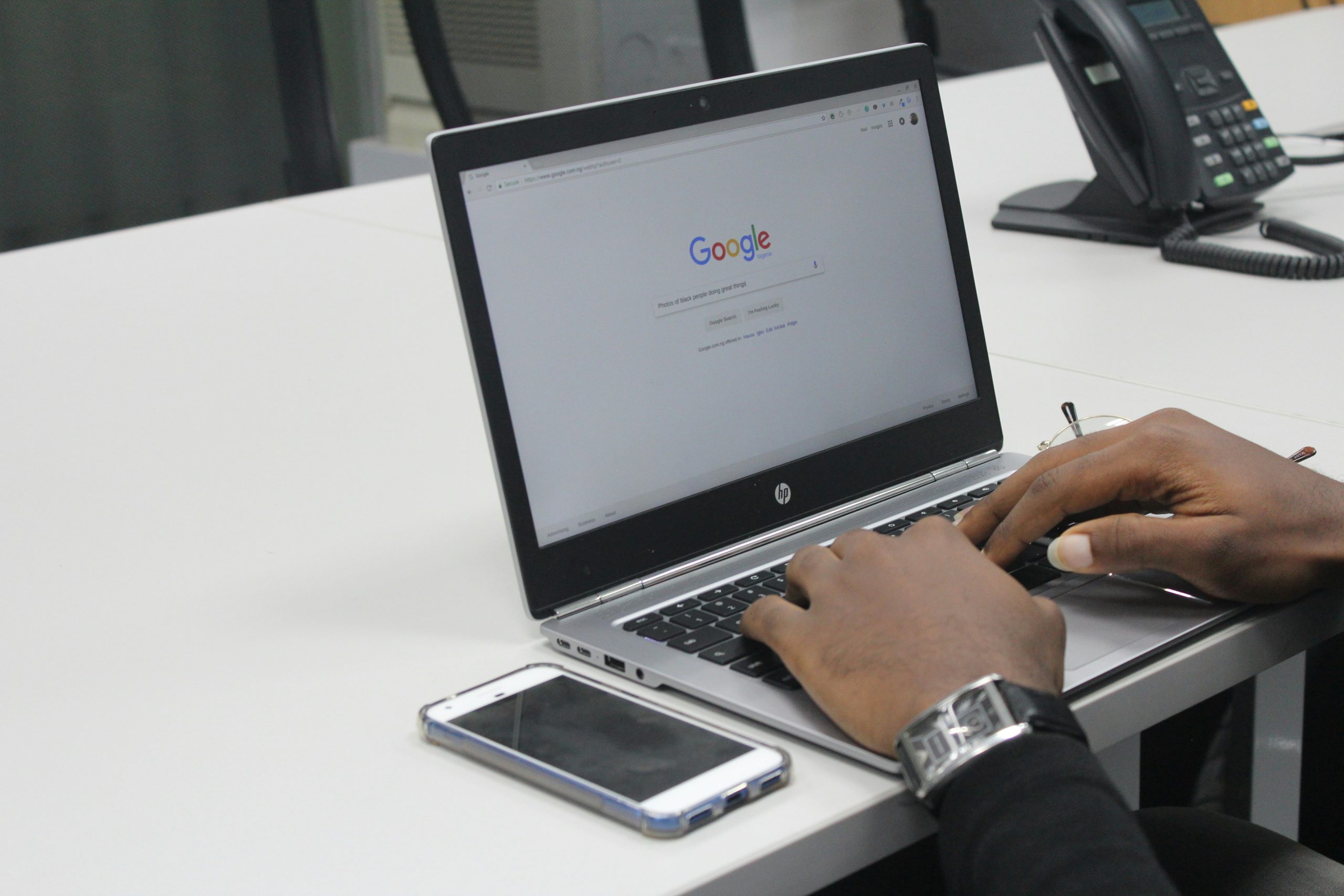 Person arbeitet an einem HP-Laptop mit geöffneter Google-Startseite im Büro, Smartphone liegt daneben.