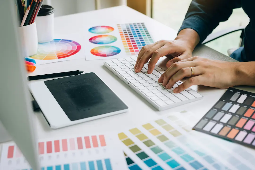 Designer arbeitet am Computer mit Farbpaletten und Grafiktablett.