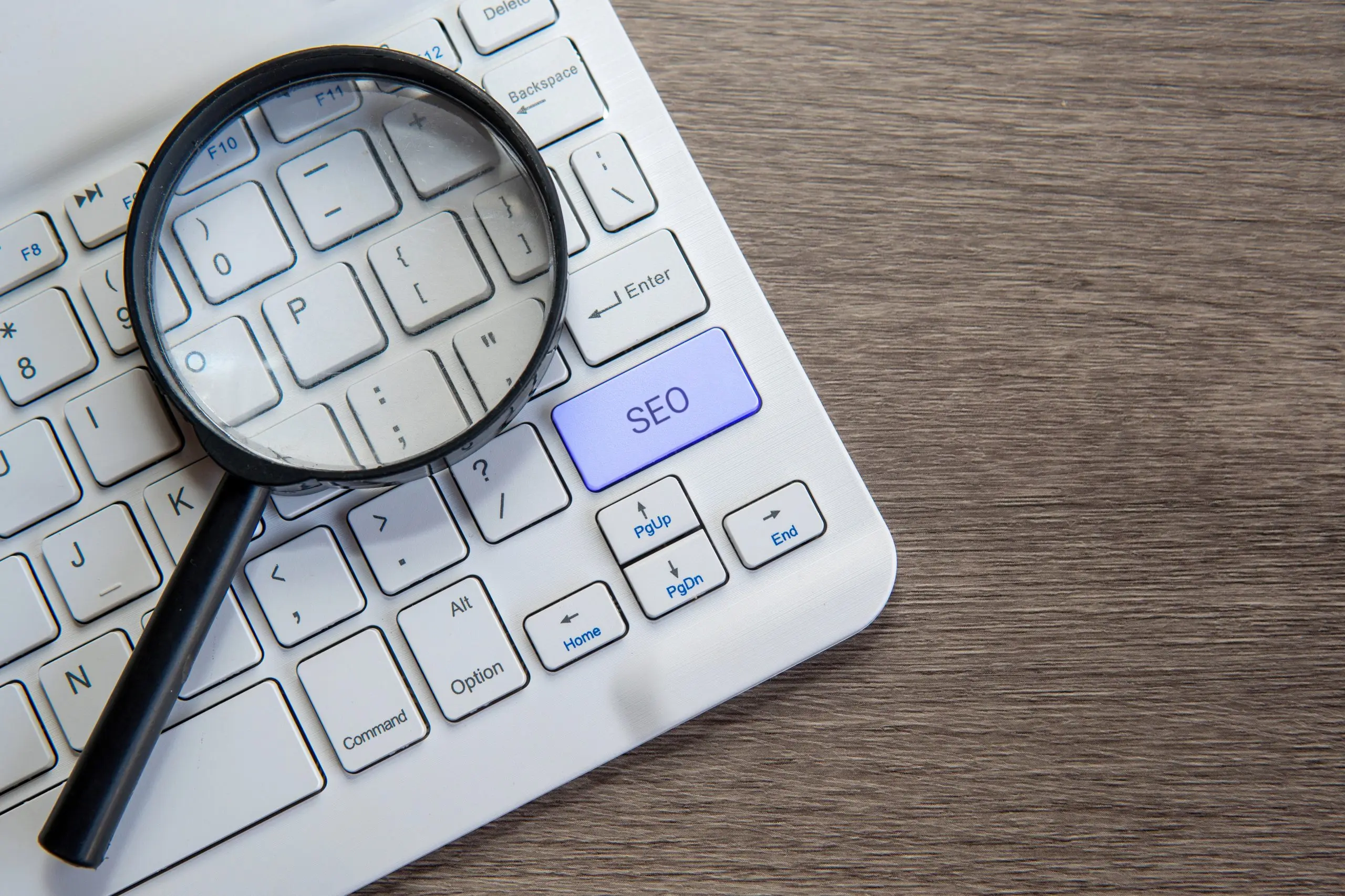 Lupe auf Laptop-Tastatur mit hervorgehobener SEO-Taste symbolisiert Keyword-Recherche