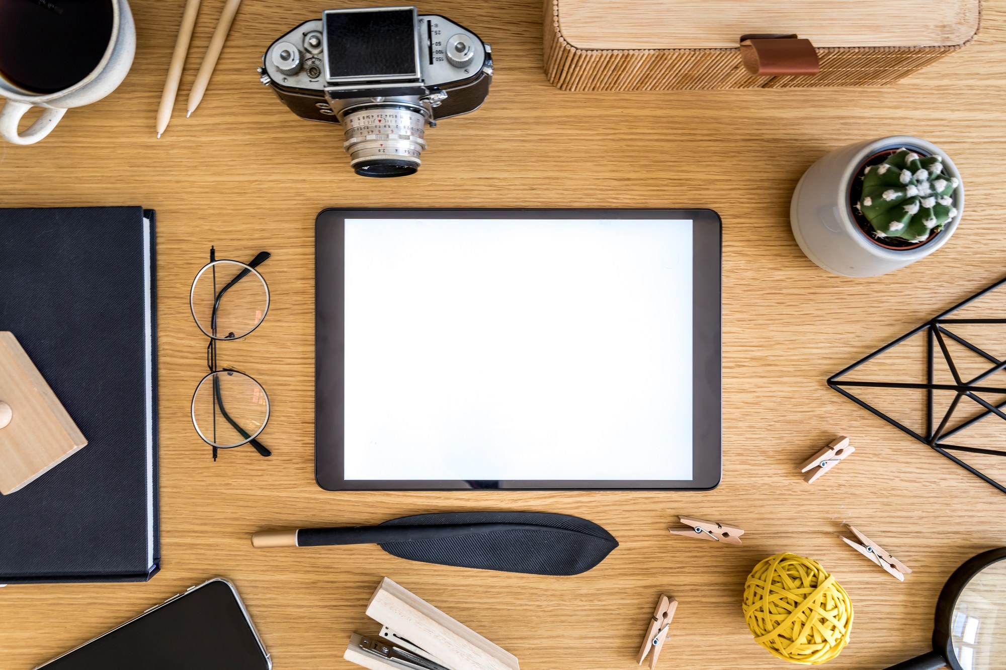 Aufgeräumter Schreibtisch von oben mit leerem Tablet, Kamera, Notizbuch und Arbeitsmaterialien