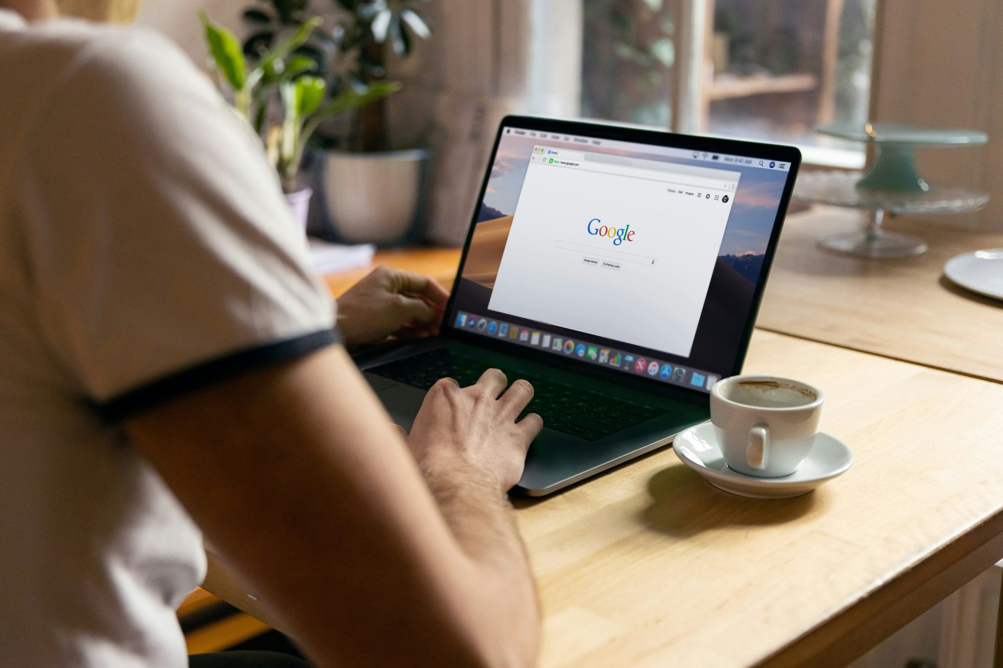 Person tippt auf Laptop mit geöffneter Google-Suche neben einer Tasse Kaffee