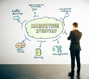 Geschäftsmann betrachtet ein Wanddiagramm mit den Bausteinen einer Marketing Strategy wie Social Media, Planning und Management