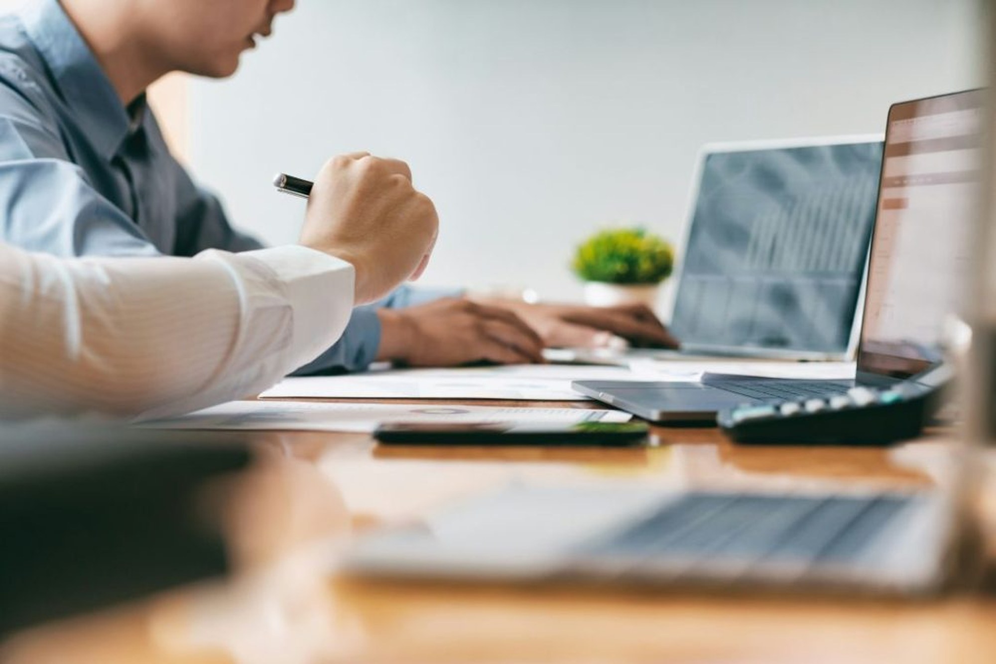 Person wertet Diagramme neben mehreren geöffneten Laptops im Büro aus