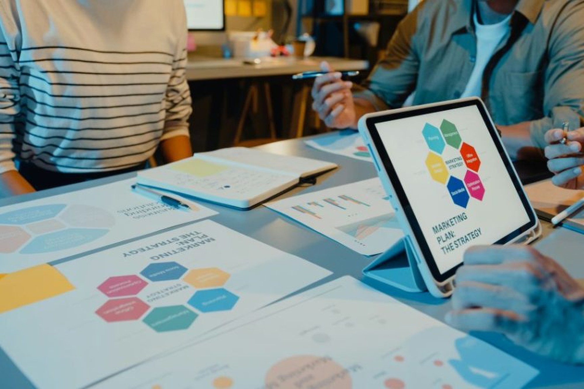 Tablet zeigt eine Marketingstrategie-Grafik neben ausgedruckten Diagrammen im Teammeeting