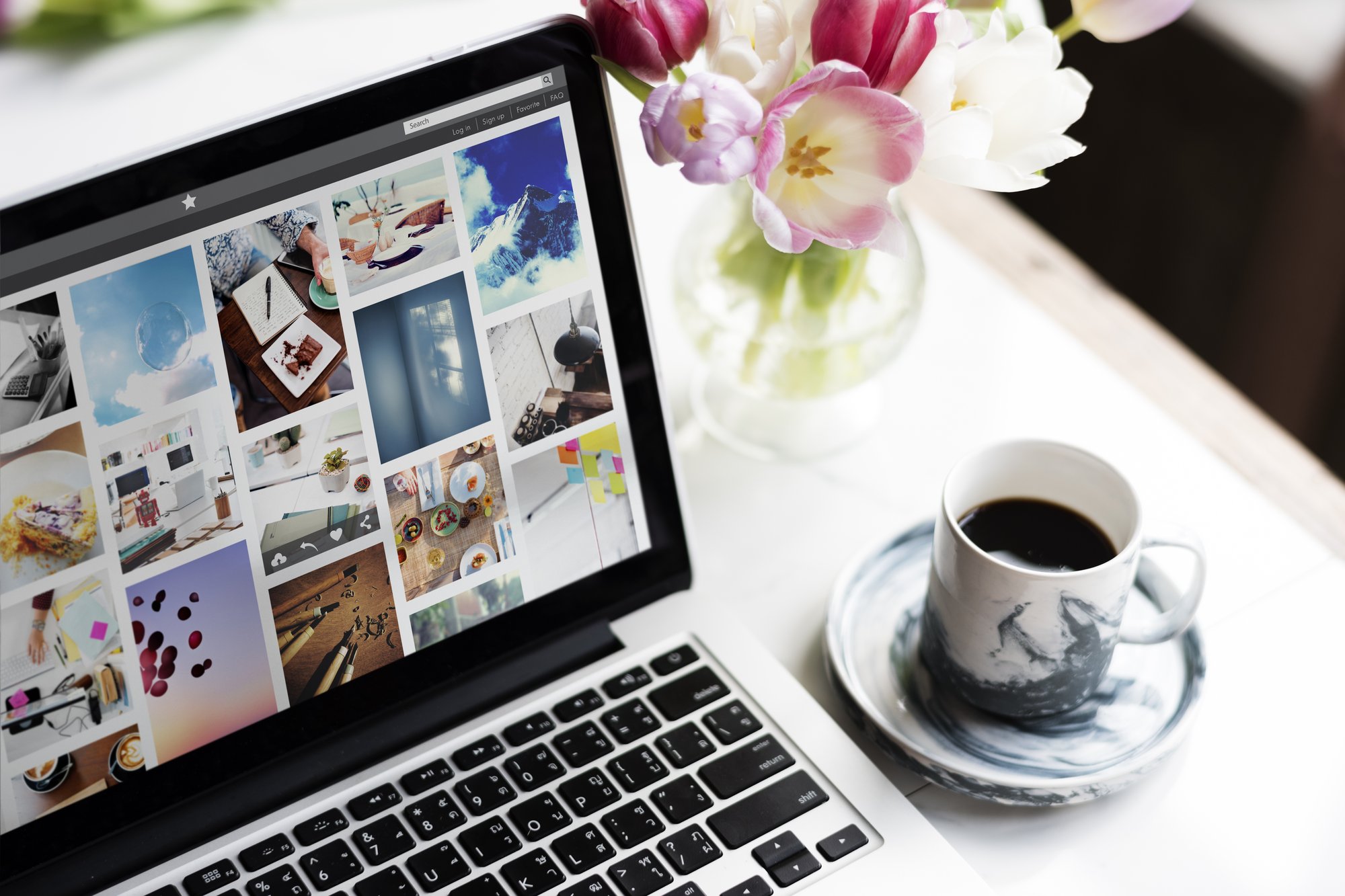 Laptop zeigt eine visuelle Bilder-Pinnwand mit verschiedenen Motiven, Tulpenstrauß im Hintergrund