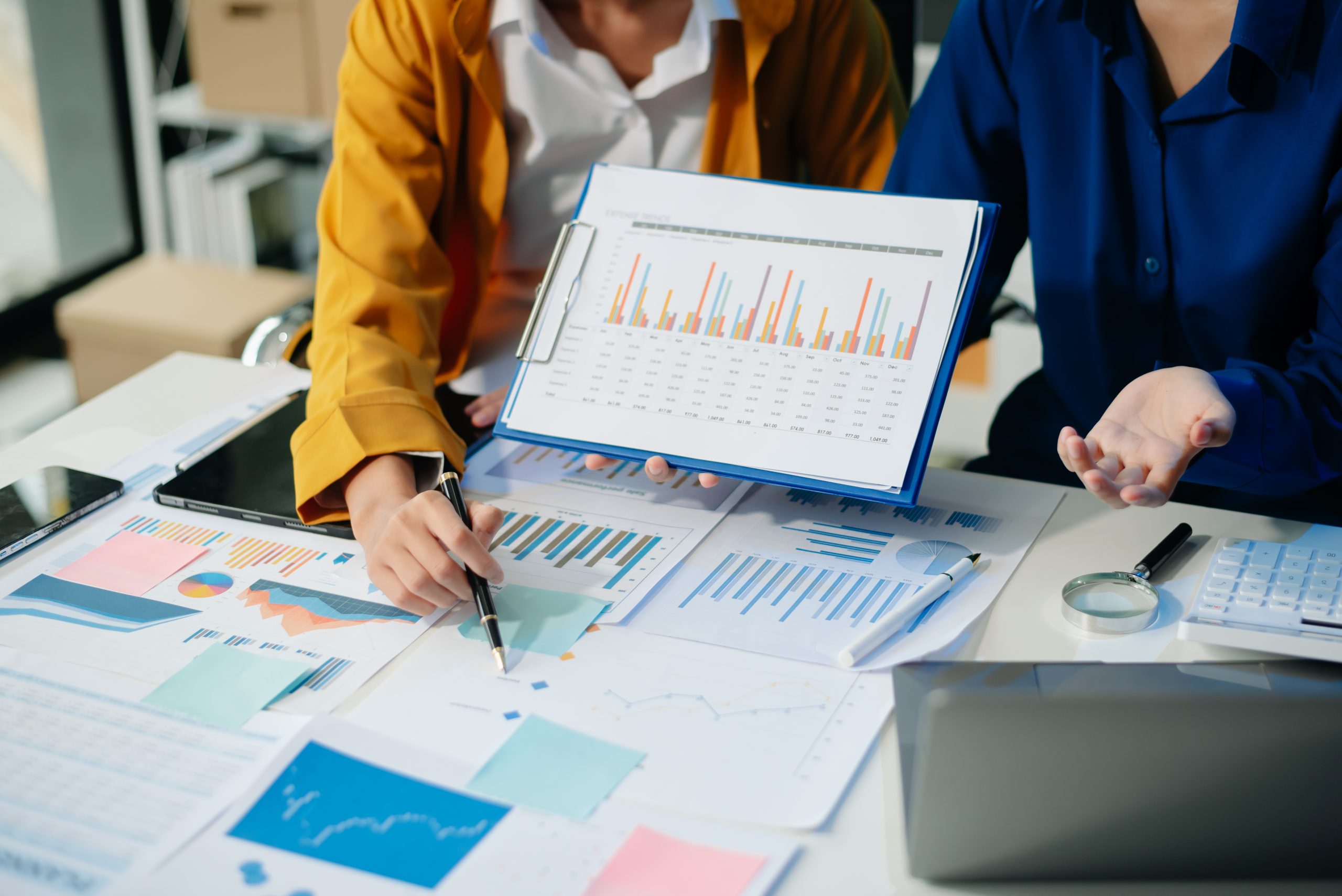 Zwei Fachleute besprechen Finanzberichte mit Balkendiagrammen und Ausgabentabellen an einem Schreibtisch