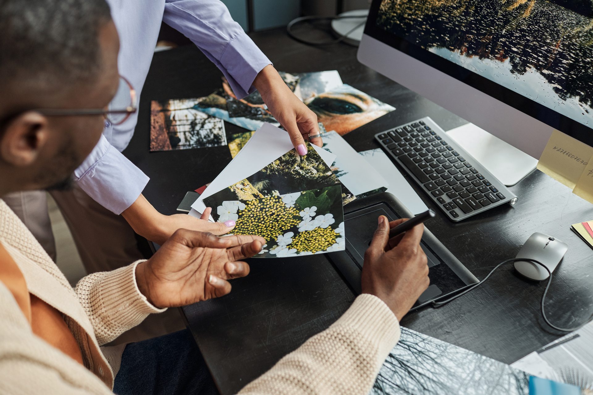 Zwei Kreative wählen ausgedruckte Fotos am Schreibtisch mit Grafiktablett aus, Motivauswahl für Snapchat-Werbeanzeigen