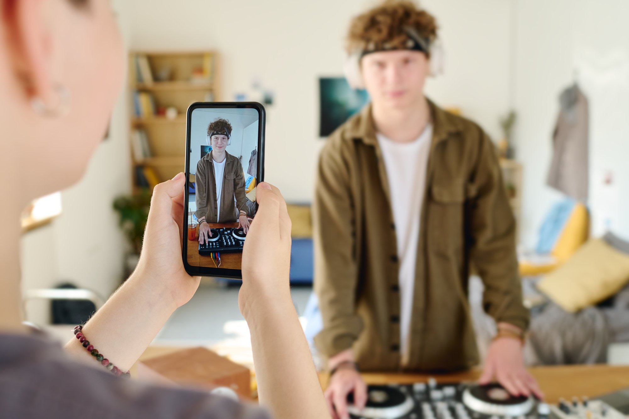 Jugendlicher filmt sich selbst mit dem Smartphone beim Auflegen an einem DJ-Mixer