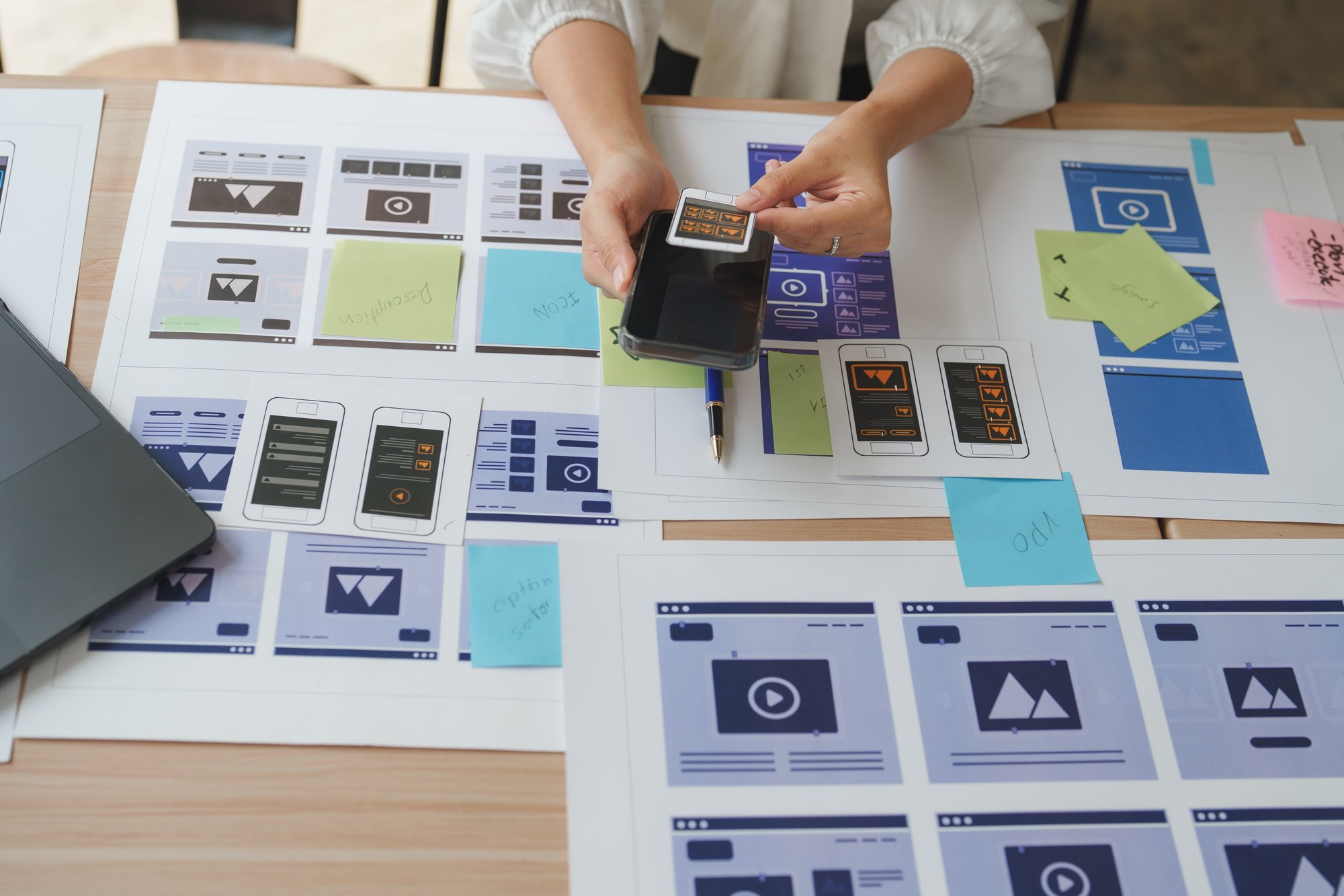 Person hält Smartphone über ausgebreitete Wireframe-Skizzen für ein Webprojekt