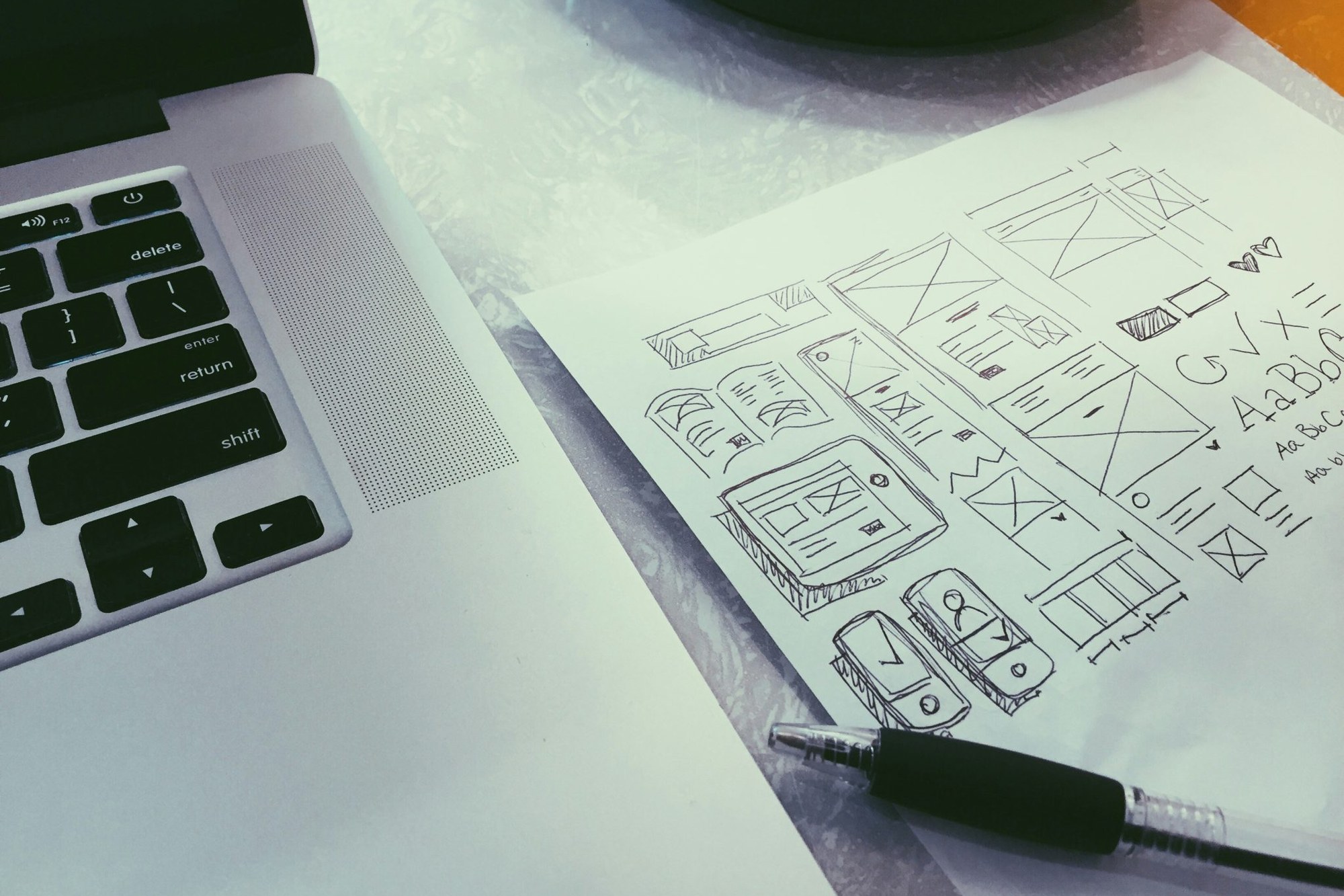 Handskizzierte Wireframes und Typografie-Notizen neben einem Laptop
