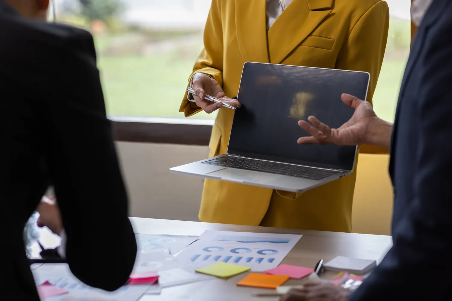 Beratungsgespräch im Büro, eine Frau zeigt mit einem Stift auf einen Laptop, Unterlagen mit Diagrammen auf dem Tisch
