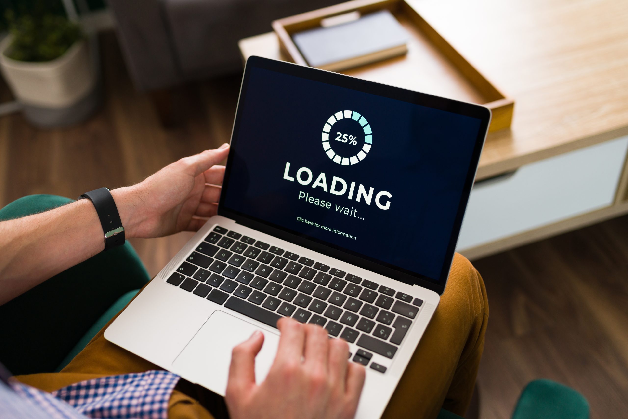Person hält einen Laptop auf dem Schoß, auf dem Bildschirm läuft ein Ladebalken bei 25 Prozent mit „Loading, Please wait“