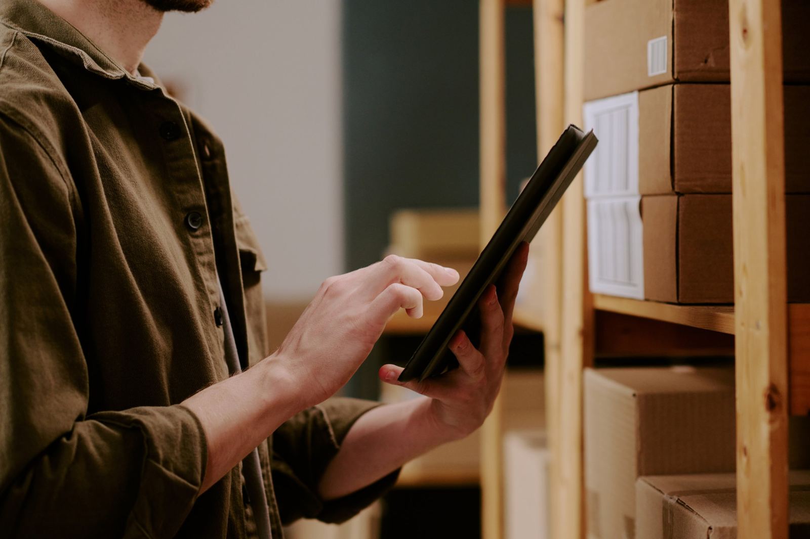 Mitarbeiter prüft den Lagerbestand auf dem Tablet vor Regalen mit Paketen – ERP- und Lageranbindung