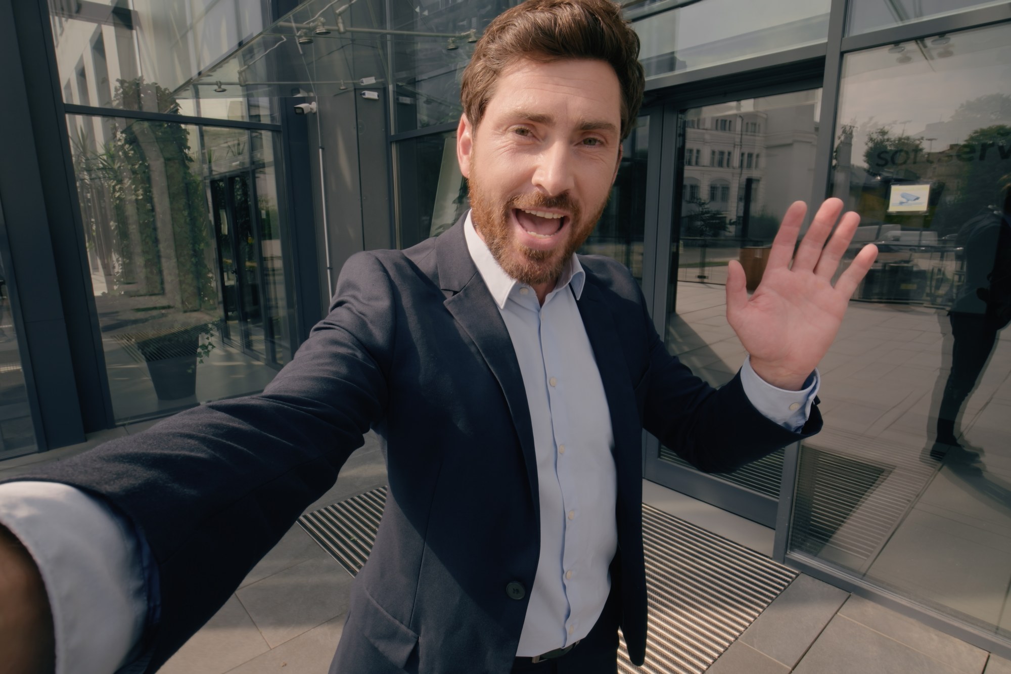 Mann im Anzug winkt in die Selfie-Kamera vor einem Bürogebäude – Hochformat-Video für Social Media