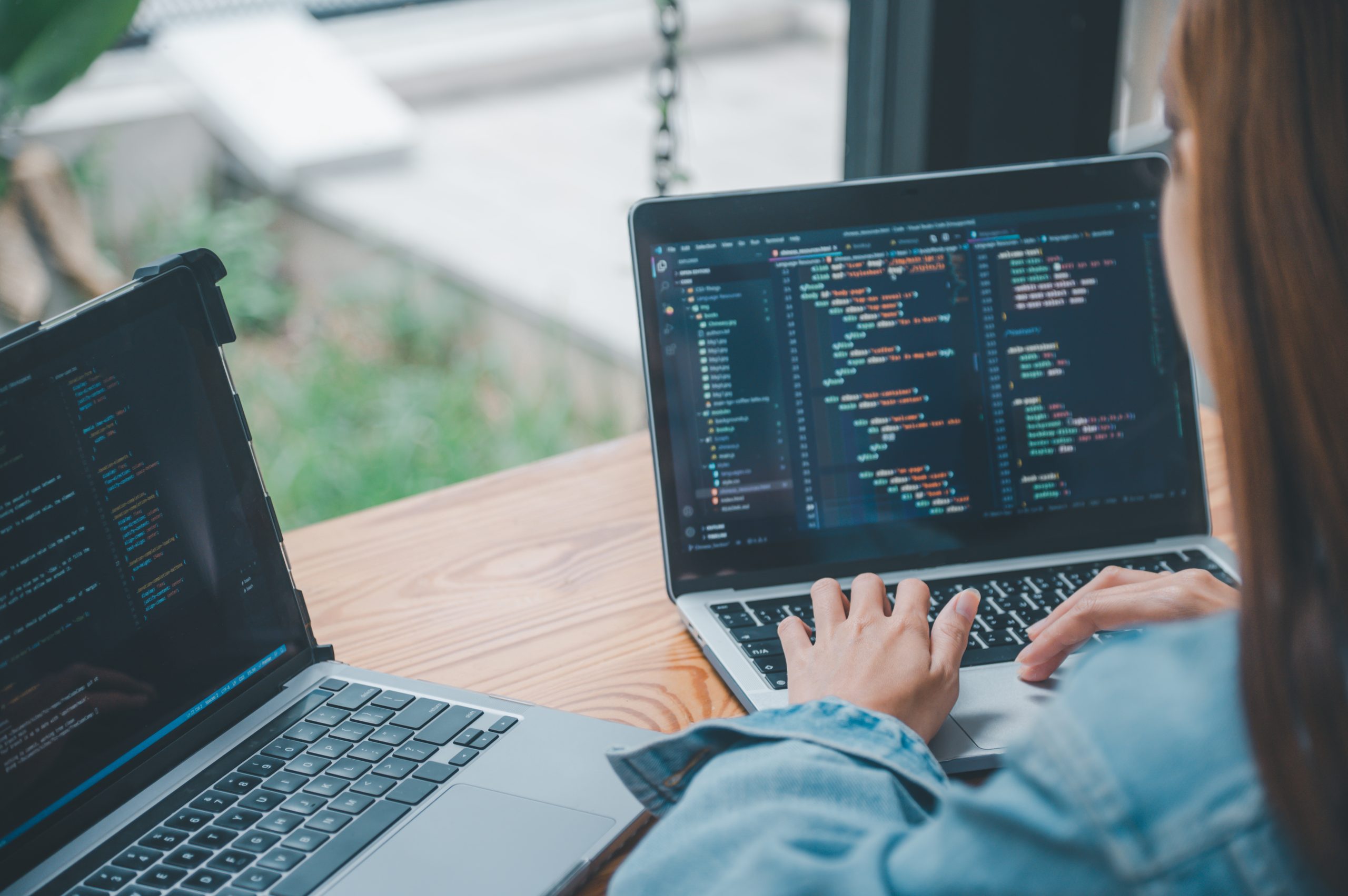 Entwicklerin arbeitet an zwei Laptops mit Quellcode – laufende Betreuung und Weiterentwicklung eines Shops